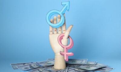 A mannequin hand holding up the male and female symbols with a pile of money strewn around